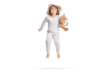Little girl in pajamas holding a teddy bear and jumping