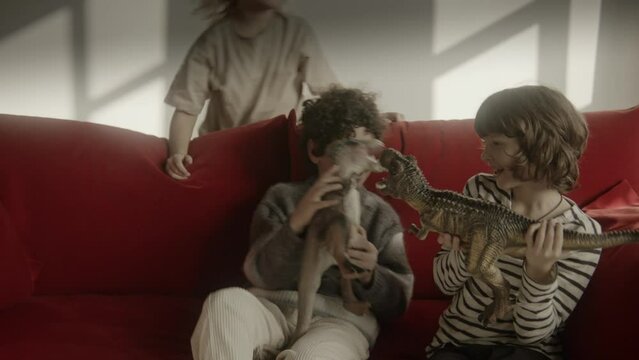 Three boys playing with dinosaur toys sitting on a red sofa