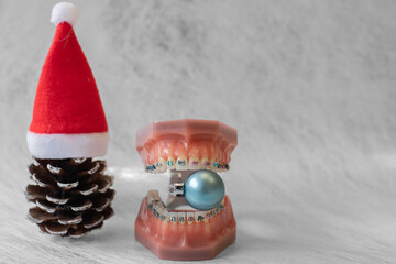 Lustiger zahnärztlicher Weihnachtshintergrund mit Platzhalter. Zahnmodell mit festsitzender Zahnspange trägt eine Weihnachtsmütze und ist eine Weihnachtskugel - obrazy, fototapety, plakaty