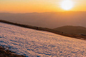 Silhouette of a woman with backpack hiking up snowy slope during sunrise from Ladinger Spitz to...