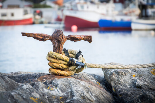 Rusty and weathered poller on a small harbour dock with a yellow rope around it