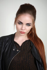 Portrait of a beautiful fashionable glamorous red-haired girl in the studio, in a leather jacket on...