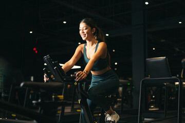 Young Asian woman on a bicycle doing spinning in the gym. Beautiful young woman exercising on gym...