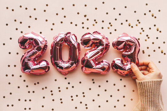 A person lays out pink New Year's air numbers of 2023 on a festive pink background. Festive background of the concept of New Year and Christmas.