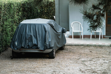 Car covering with tarpaulin material is parked at backyard. Transport care and protection concept.