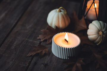 Fototapeta na wymiar Cozy autumn composition with aromatic candle, pumpkins, wool sweater, leaves, cinnamon. Aromatherapy on a grey fall morning, home atmosphere of cosiness and relax. Wooden background close up.