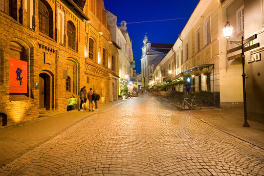 Night view of illuminated Pilies Street in the Old Town of Vilnius, Lithuania. Church of St. Johns in the background.