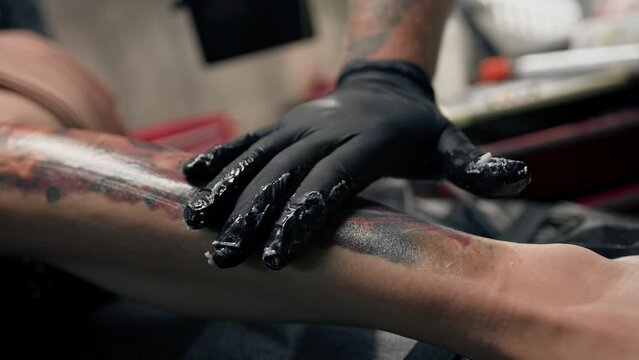 Male tattoo artist smears ointment on a tattoo after a session for quick healing, tattoo studio