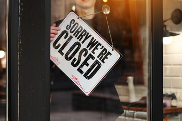 Young owner man turning signboard to closed coffee shop, owner close store or restaurant temporary due pandemic of coronavirus, lockdown, quarantine of COVID-19, war in Ukraine.