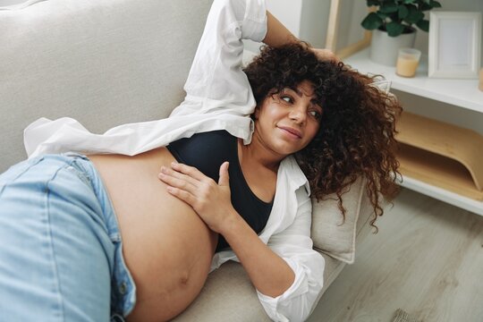 Pregnant woman smile and happiness lies on the couch freedom and strokes her belly feels kicks with the baby in the last month of pregnancy, mother's day lifestyle