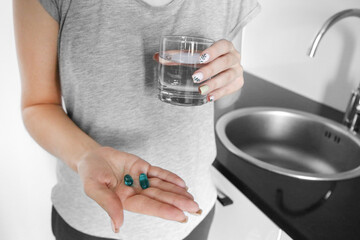 girl holding pills drinks water in the kitchen. Vitamins. Disease. Contraceptive. Unhealthy. Treatment