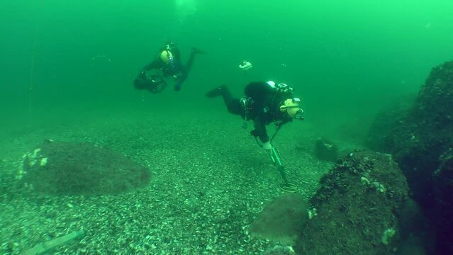 Underwater archaeological research: Divers with a metal detector explore the seabed among rocks, wide shot.