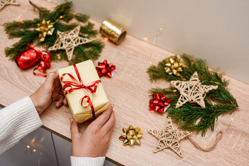 Female hands wrapping christmas gift box above wooden table.