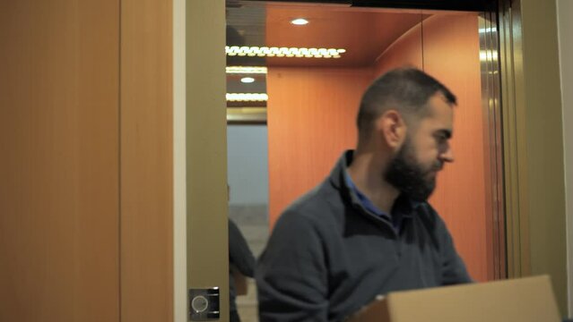 Delivery Man Stepping Out Of An Elevator Carrying A Parcel On His Hands.