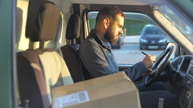 Delivery man working inside a van holding a tablet next to a parcel ready to deliver.