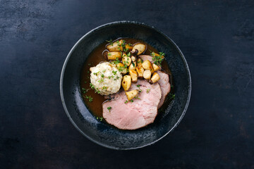 Fototapeta na wymiar Traditional German pork roast served with bread dumpling and king oyster mushroom in dark beer sauce served as top view in a Nordic design bowl with copy space