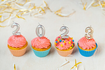 Food concept of New year 2023. Festive cupcakes and candles in form of numbers 2023 on white background.