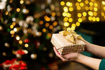 Young woman holding a gift box against the background of Christmas decor and gifts, close-up.