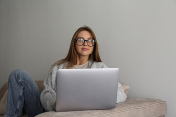 Close up shot of young smiling woman working remotely from home on laptop, sitting on the couch in living room. Female freelancer in blue light glasses with hands on keyboard. Copy space, background.