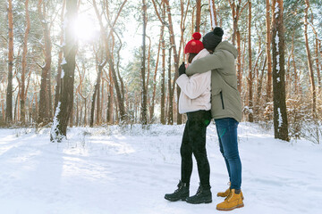 Young happy couple on sunny day in snow-covered park. Men and women are standing and hugging in a snowy winter park. Side view