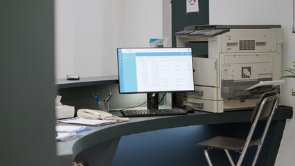 Reception counter in health center to make appointments on computer, giving medical support to patients. Empty hospital registration desk with report papers and checkup forms. Handheld shot.