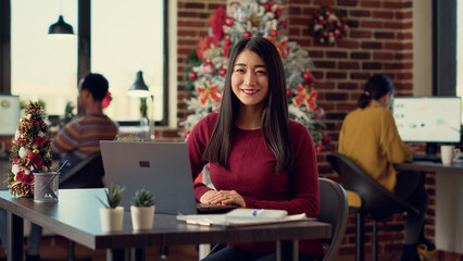 Portrait of female worker using laptop in festive office filled with winter decorations and...