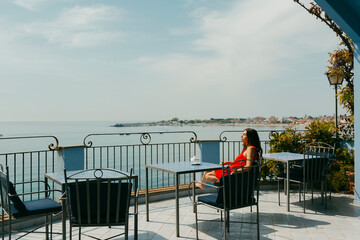 Girl enjoying morning sun while having tea in hotel terrace by the sea