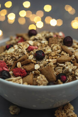 A bowl of muesli on a gray monochrome background, with white feathers and a side from a garland. Healthy food, healthy breakfast