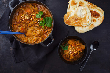 Traditional Indian vegetarian Madras curry stew with sweet potatoes, roasted cashew nuts and garlic chapati bread served as top view in a design bowl and a rustic pot
