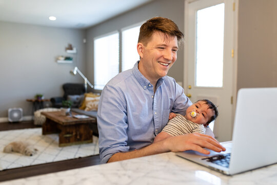 Man Mutiltasks Working On Laptop While Holding A Baby