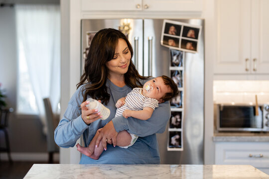 Mother Prepares A Bottle In The Kitchen While Holding Child