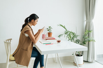 millennial woman with mobile phone making notes preparing to exams
