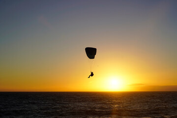 Silhouette of a parachute during sunset, over the beach 