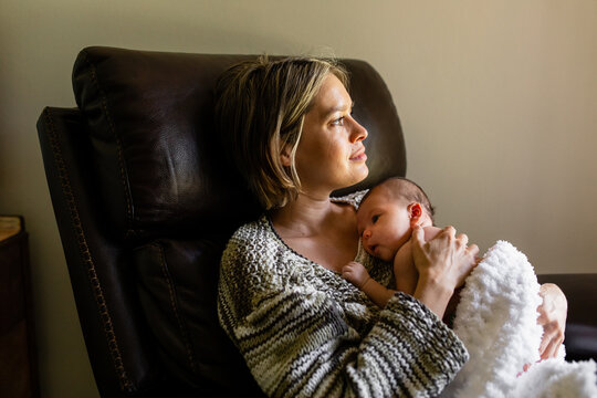 Mother Looks Out The Window As She Holds Her Newborn Baby