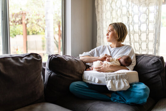 Mother Looks Solemnly Out The Window While Breastfeeding Infant