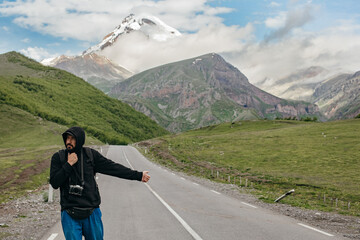 A traveler hitchhiking on the road near the beautiful mountains