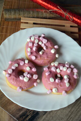 Three donuts with pink icing on a plate on a wooden table. Sweet breakfast.