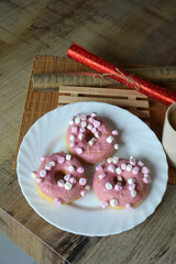 Three donuts with pink icing on a plate on a wooden table. Sweet breakfast.