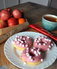 Cup of black tea with lemon and three donuts with pink icing on a plate on a wooden table. Sweet breakfast.