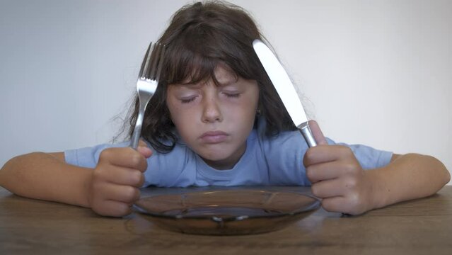 Food shortage and empty plate indoor. A child sits hungrily by the empty plate during food shortage time in the world.