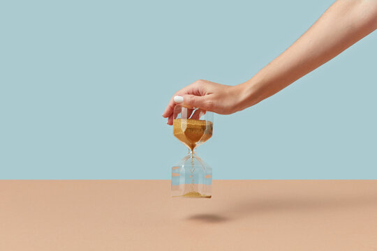 Sandglass with golden sand in female hand.