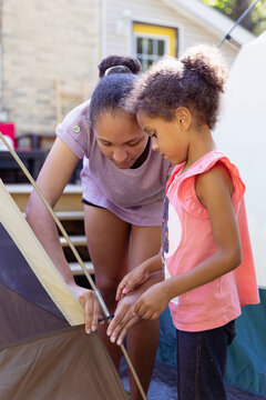 Teenager showing her young sister how to assemble a tent