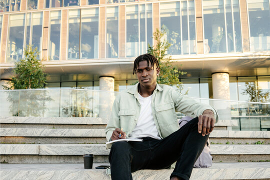Portrait of male student sitting on stairs outside university building