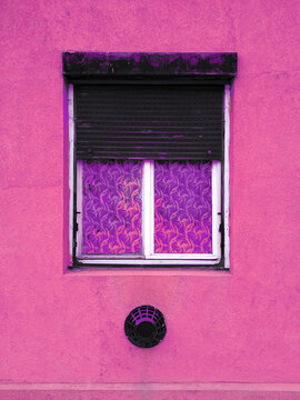 A half-down rusty sunblind on the window of a vintage old pink house.