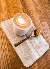 cup of coffee with latte art on wooden board and a golden spoon next to it, a flat white with a golden spoon, a cafe latte with a wooden background, latte macchiato high angle shot, cappucino 