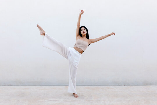 Asian ballerina dancing against gray wall