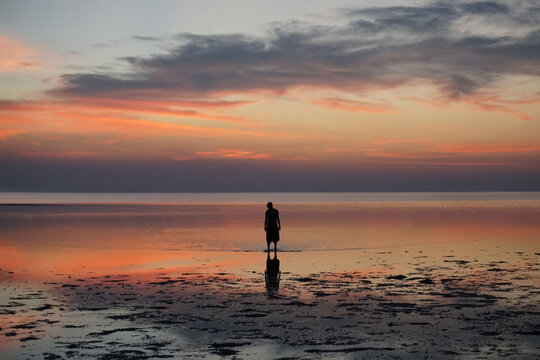A man standing in the colorful water during sunset in Thailand