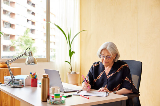 Focused mature woman writing on paper in office