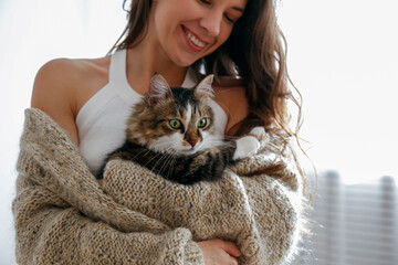 Portrait of young woman holding cute norwegian cat with green eyes. Female hugging her cute long...