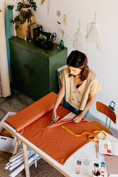 A standing woman cuts a piece of cloth on the table.